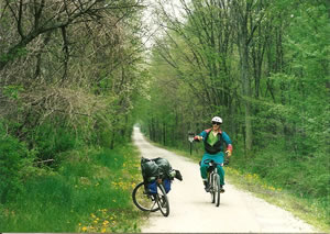 Terry cycling the Kal-Haven bike trail next to Ted's parked bike. Both bikes are loaded with camping gear. 