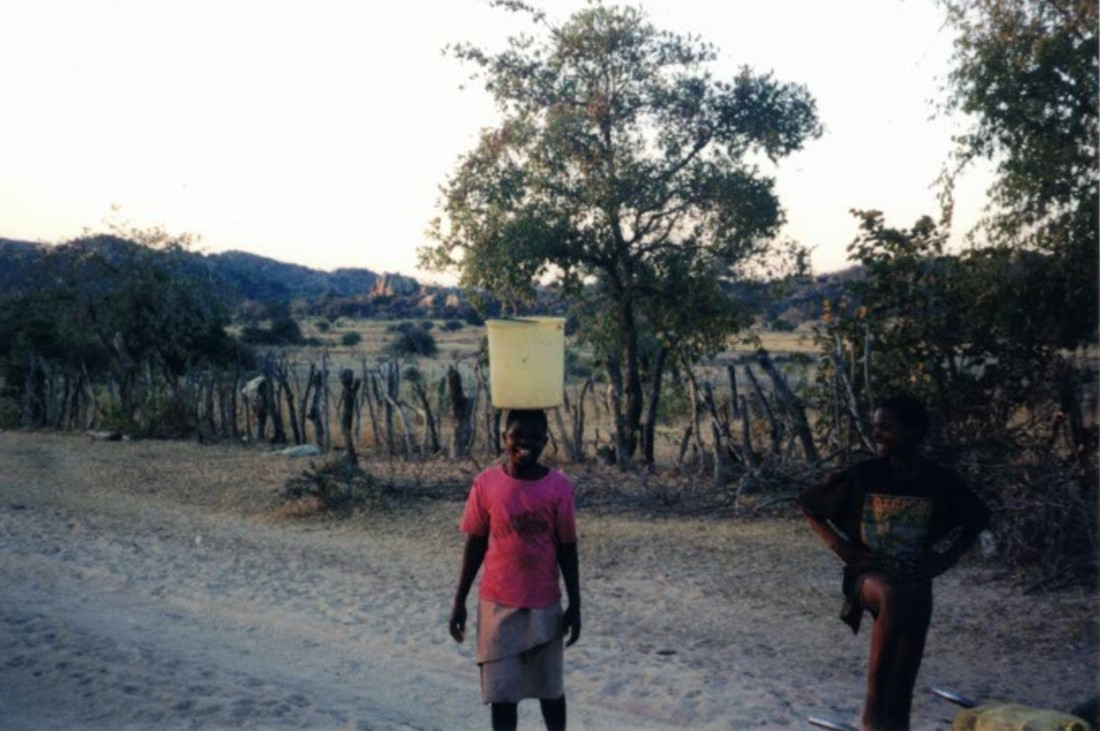 A woman balancing a bucket full of water on her head.