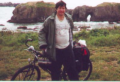 Ted with his bike in front of rocky coast in Bandon, Oregon.