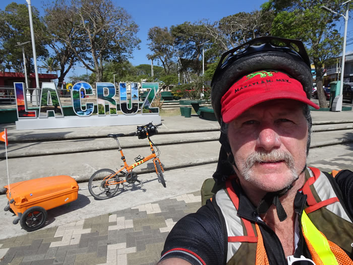 Ted with his bike in front of the La Cruz sign at the park in La Cruz, Costa Rica.