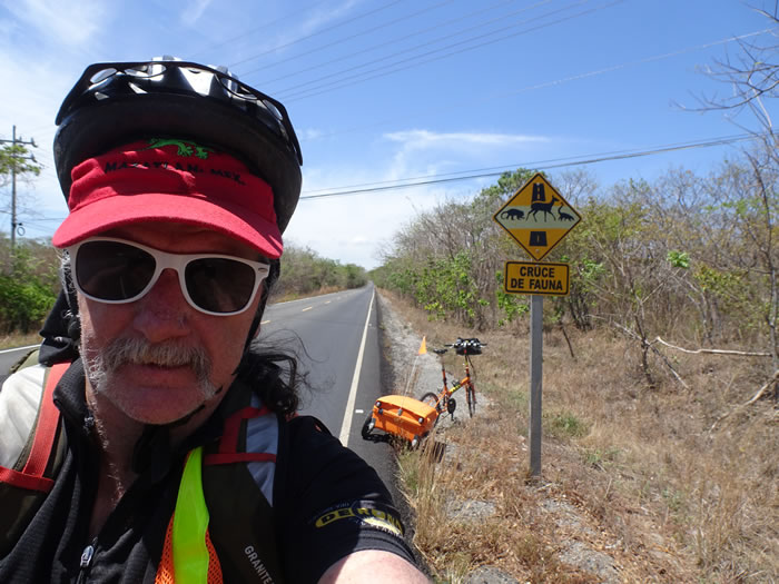 Ted with an animal crossing sign and his bike behind him.  This is on the Pan American highway between La Cruz and Liberia, Costa Rica.