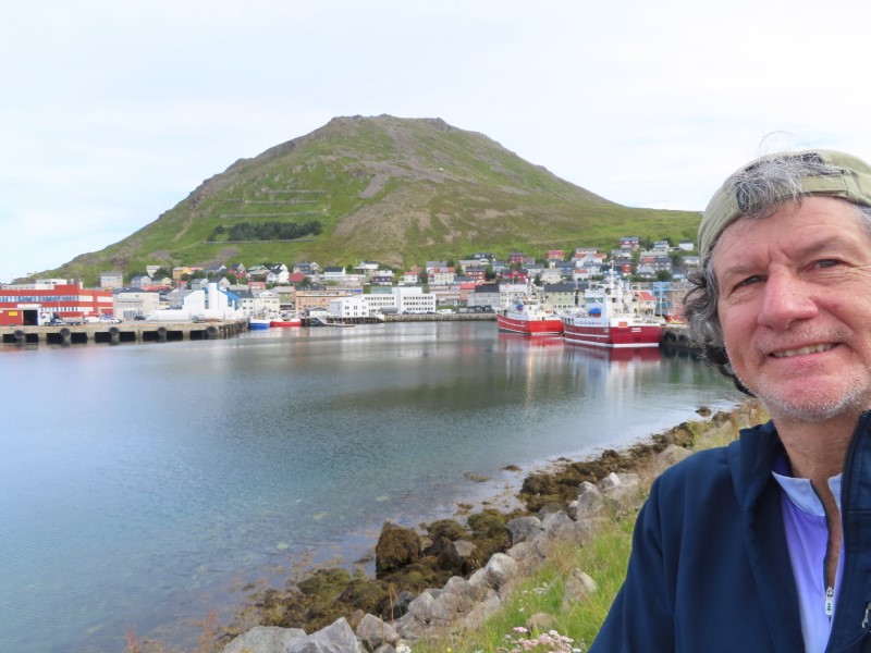 Ted with the town of Honningsvåg, Norway and hill behind him that he hiked half way up.