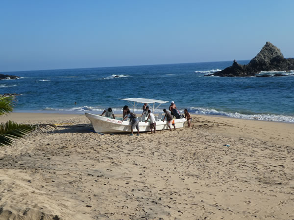 People pushing a boat onto the shore at Mazunte, Mexico.